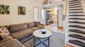 A living room with a sofa, a coffee table with flowers, a staircase, and a kitchen in the background. - Nice home in Alingsås (Alingsås)