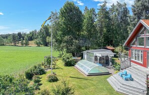 Ett hus med en röd fasad, ett stort växthus och en terrass med blå stolar.