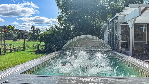 A swimming pool with a waterfall feature, surrounded by a garden and a building with large windows. - Nice home in Alingsås (Alingsås)