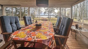 Een overdekt buitenruimte met een lange tafel, stoelen en uitzicht op een bebost landschap.