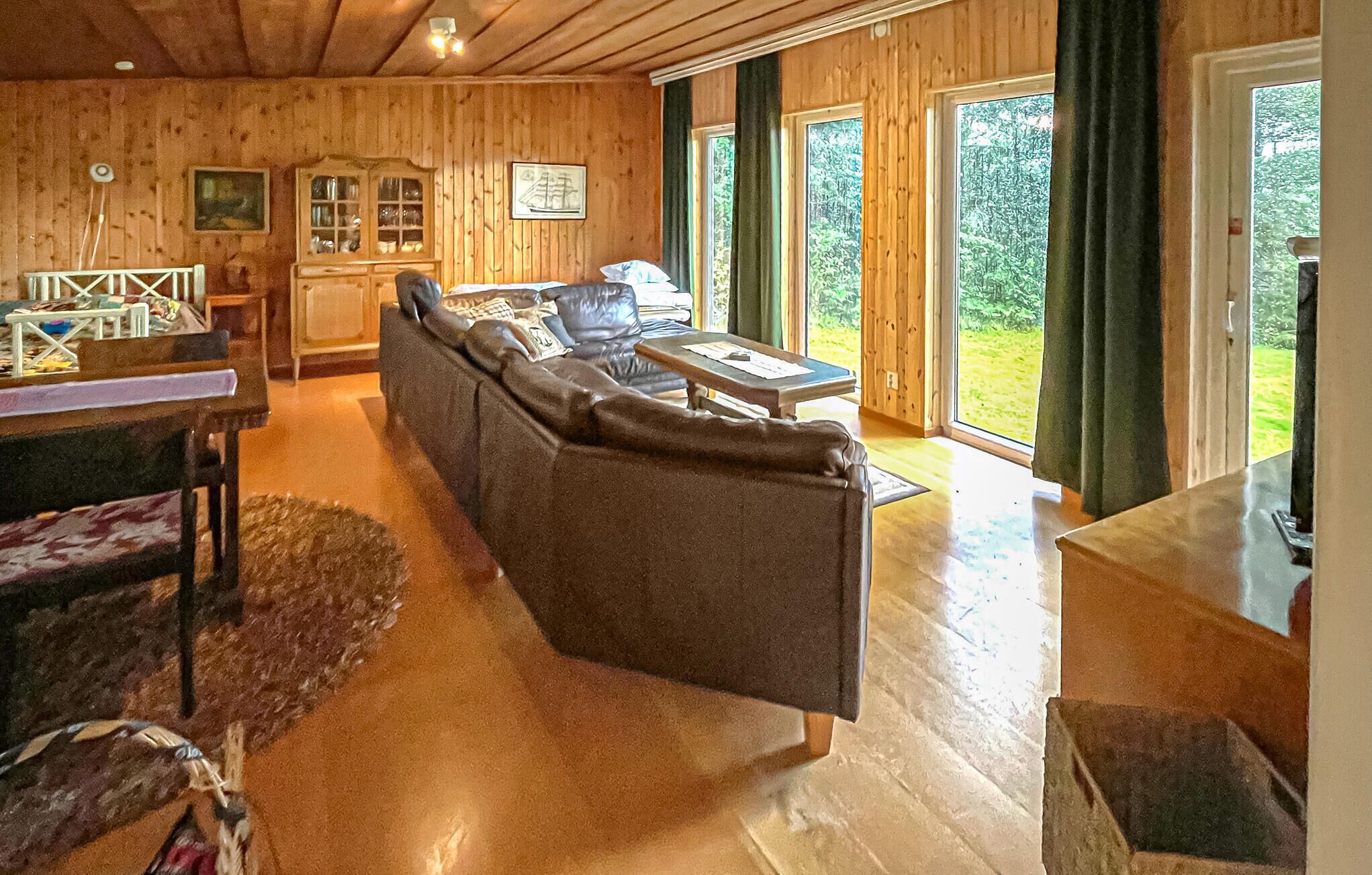 A cozy cabin interior with a sofa, dining table, and large windows offering a view of the outdoors.