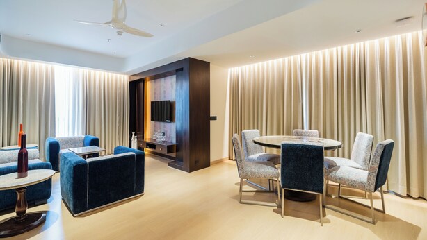 A modern hotel room with a dining area, a flat-screen TV, and a ceiling fan. - Akaya Elegance (Ahmednagar)