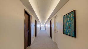A long, narrow hallway with doors on both sides, a carpeted floor, and a ceiling with recessed lighting. - Akaya Elegance (Ahmednagar)