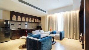A modern living room with a sofa set, a coffee table, and a kitchen area with a refrigerator and cabinets. - Akaya Elegance (Ahmednagar)