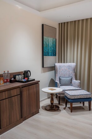 Una habitación moderna con un escritorio de madera, una silla, una mesita pequeña y un ventanal con cortinas.