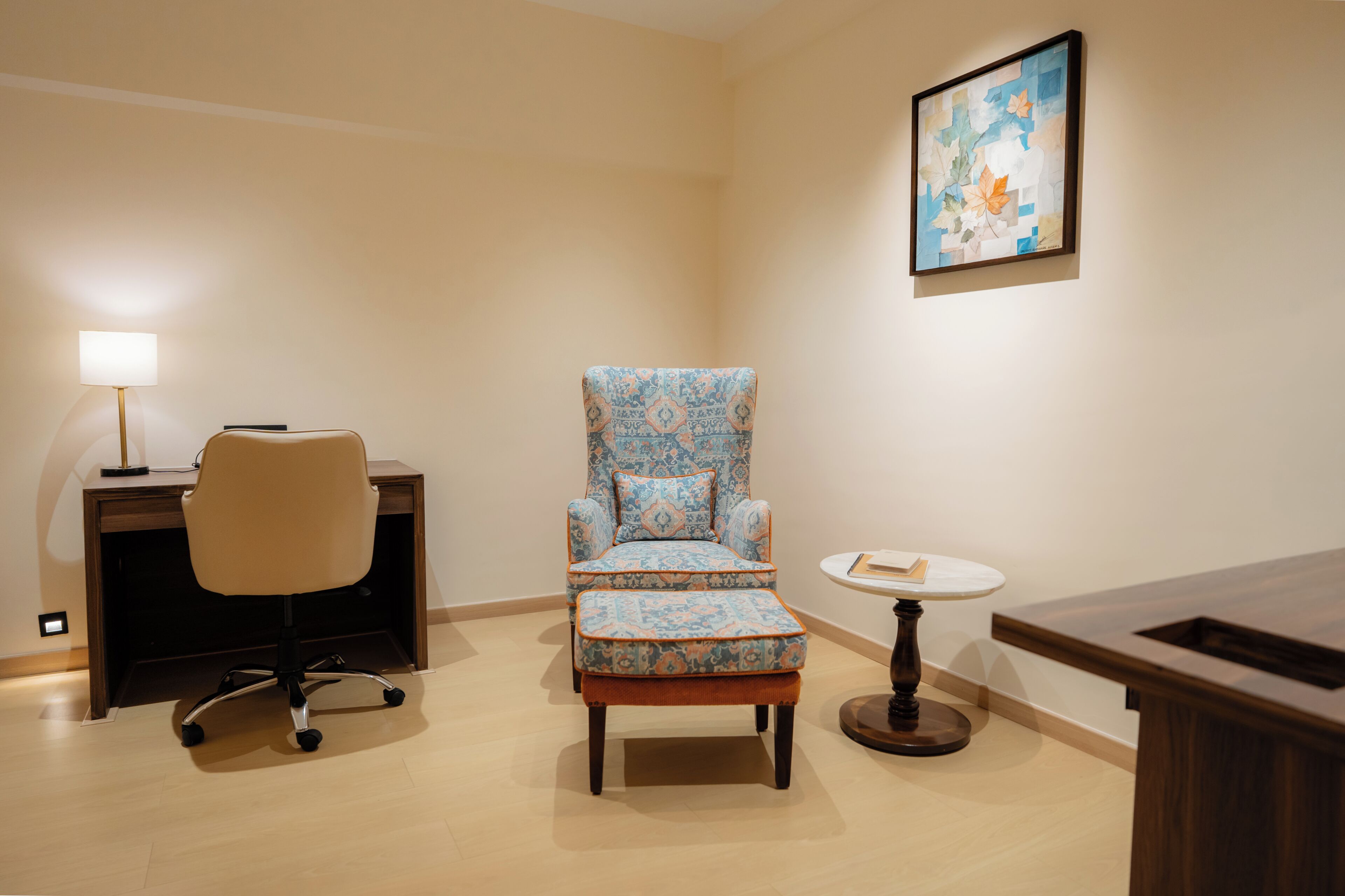 A room with a desk, a chair, a small table, and a framed picture on the wall.
