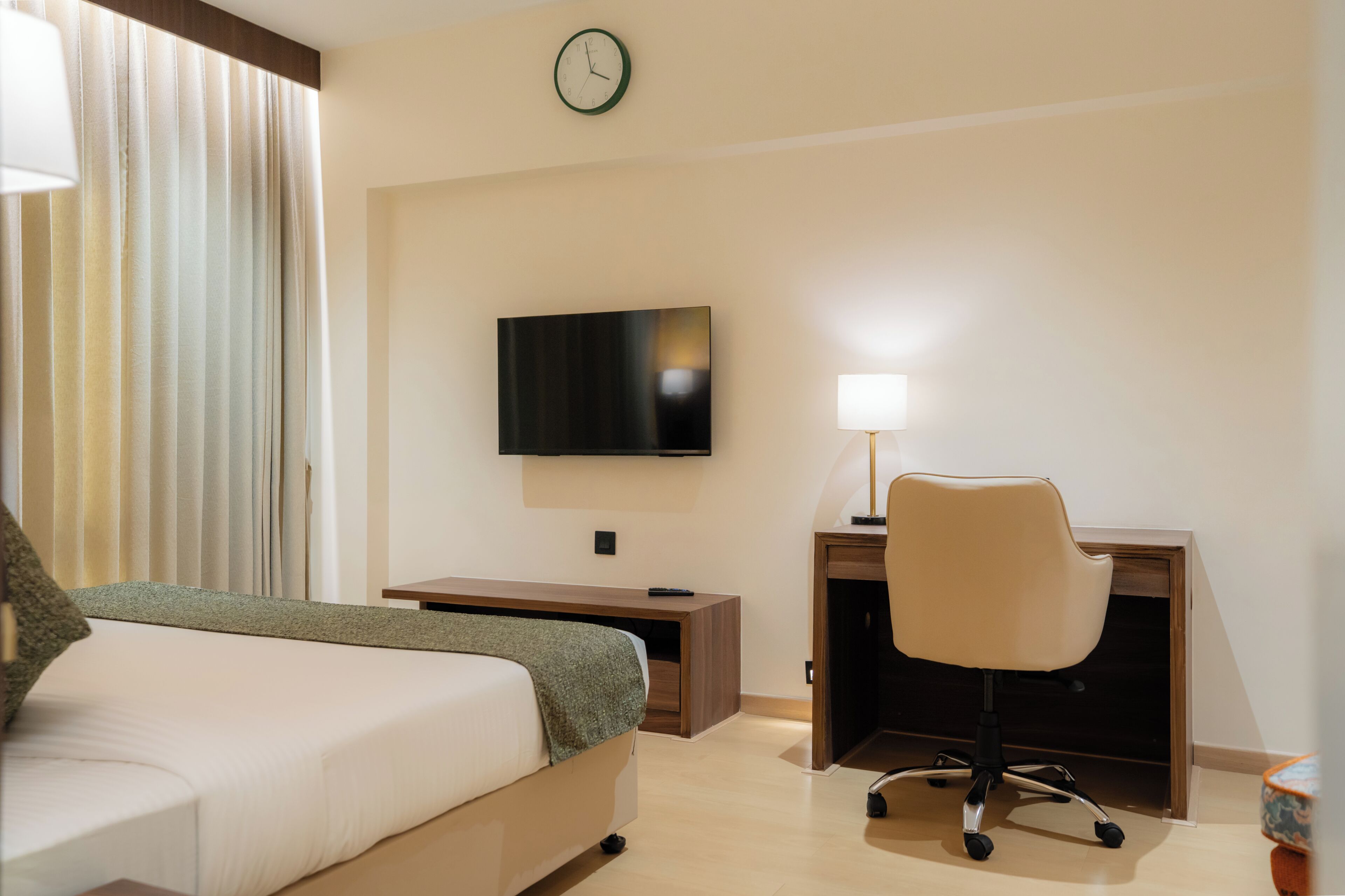 A hotel room with a bed, desk, chair, TV, lamp, and curtains.