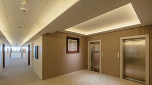 A hotel corridor with a carpeted floor, wooden panel walls, and two elevators. - Akaya Elegance (Ahmednagar)