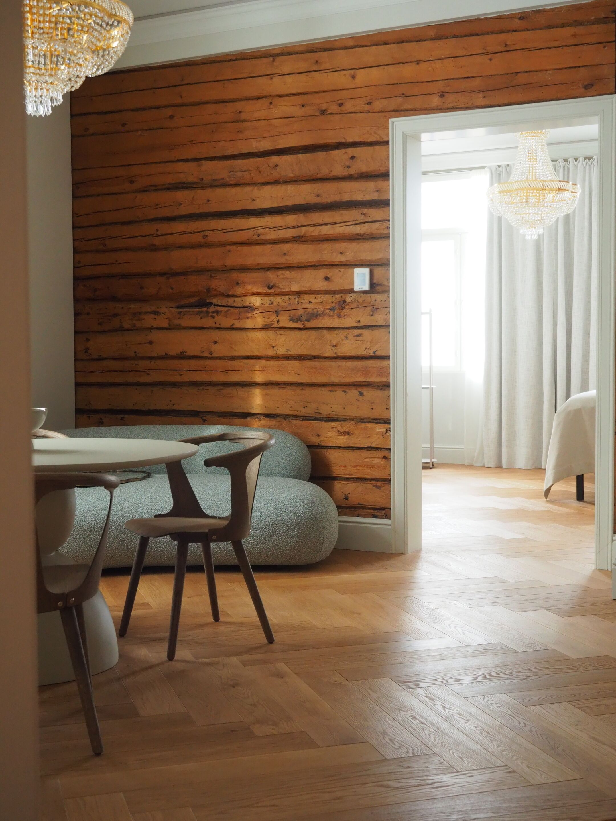 A dining area with a wooden wall, a chandelier, and a view into another room.