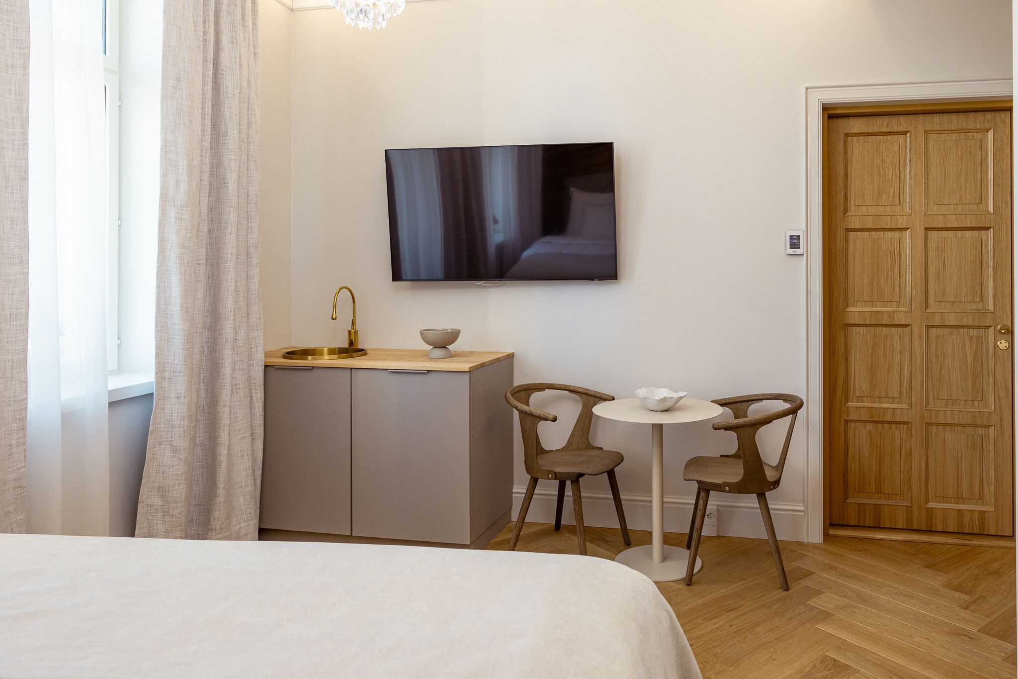 Hotelkamer met een bed, een aan de muur bevestigde televisie, een kleine kitchenette en twee stoelen rondom een tafel.