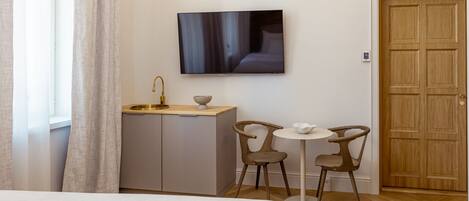 Hotelkamer met een bed, een aan de muur bevestigde televisie, een kleine kitchenette en twee stoelen rondom een tafel.