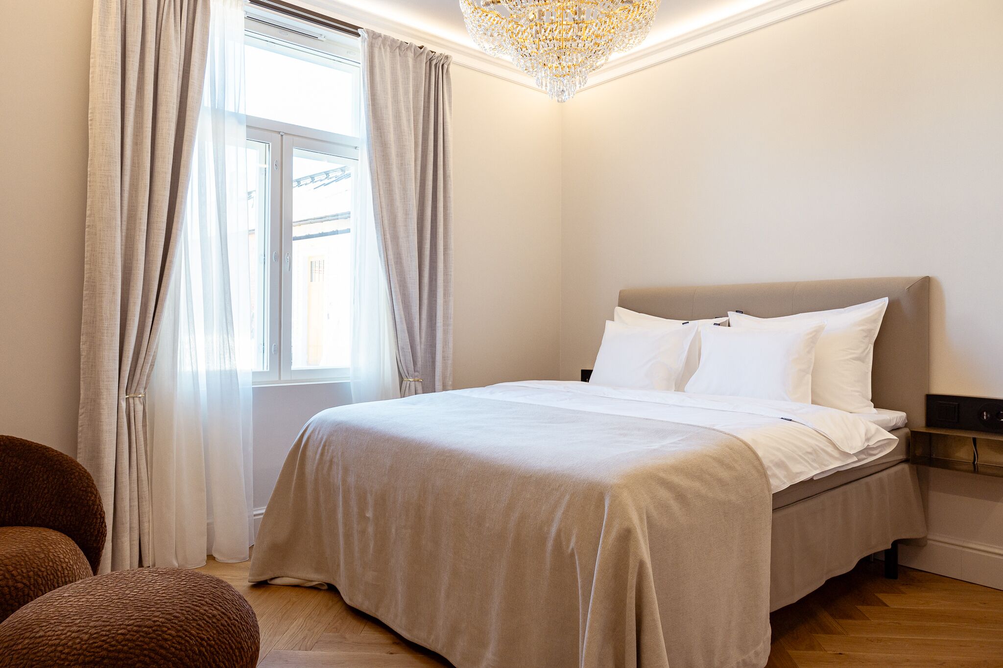 A bedroom with a bed, curtains, a chandelier, and a view of the outside.
