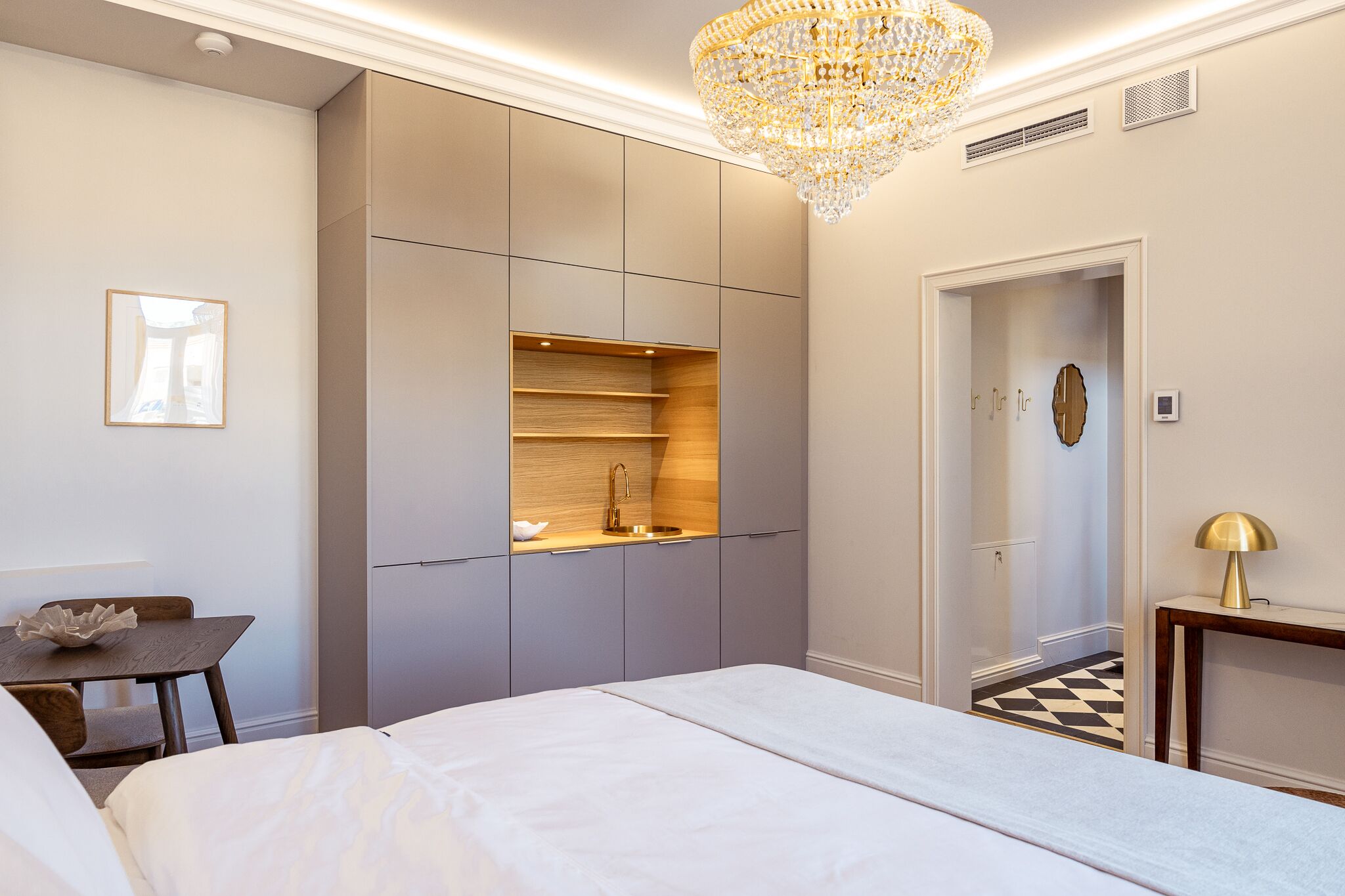 A modern bedroom with a bed, a desk, a built-in wardrobe, and a chandelier.