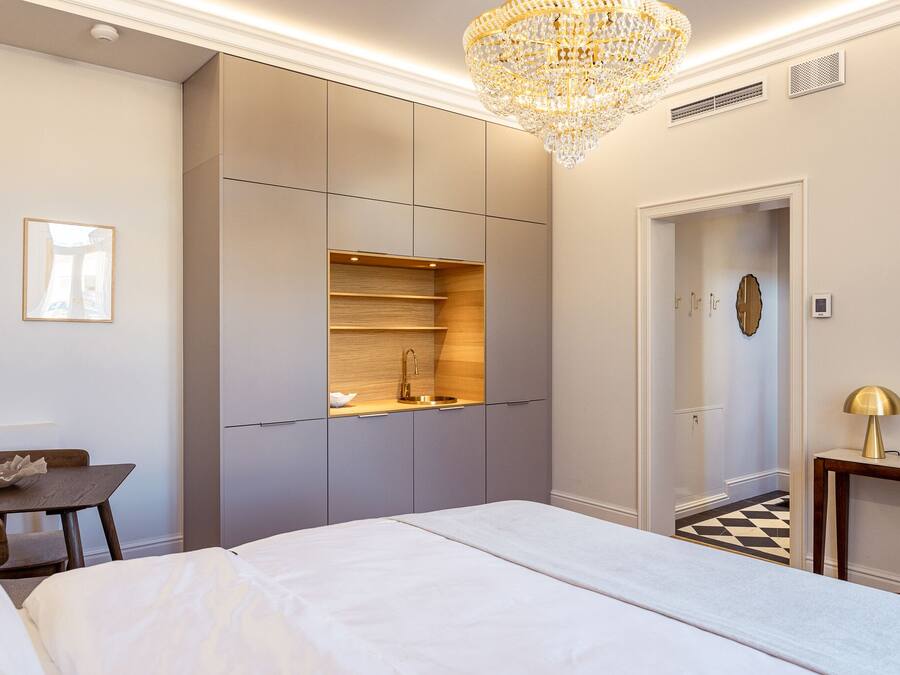 A modern bedroom with a bed, a desk, a built-in wardrobe, and a chandelier.