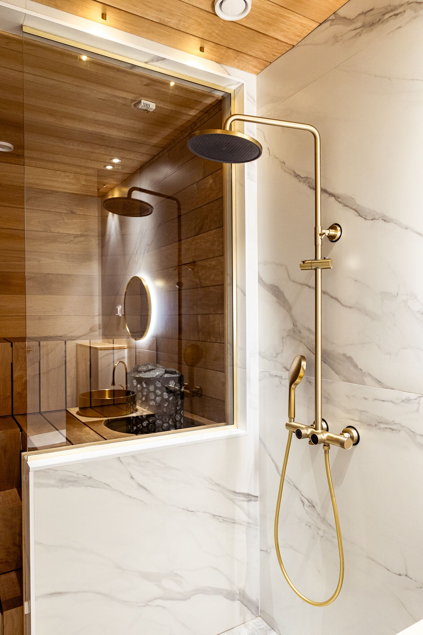 A modern bathroom with a glass enclosure, a gold showerhead, and a marble wall.