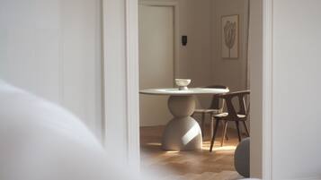 Un coin repas minimaliste avec une table ronde et deux chaises, une porte donnant sur une autre pièce et une estampe botanique encadrée au mur.