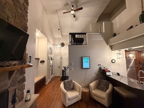 A compact living space with a stone accent wall, a ceiling fan, a flat-screen TV, a kitchen area, and two armchairs. - Family-Friendly 4BR Near Big Boulder w Lake & Mountain Access + Fireplace + Pets (Lake Harmony)