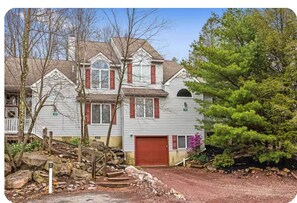 A two-story house with a red door, a front porch, and a small garden area with rocks and plants. - Family-Friendly 4BR Near Big Boulder w Lake & Mountain Access + Fireplace + Pets (Lake Harmony)