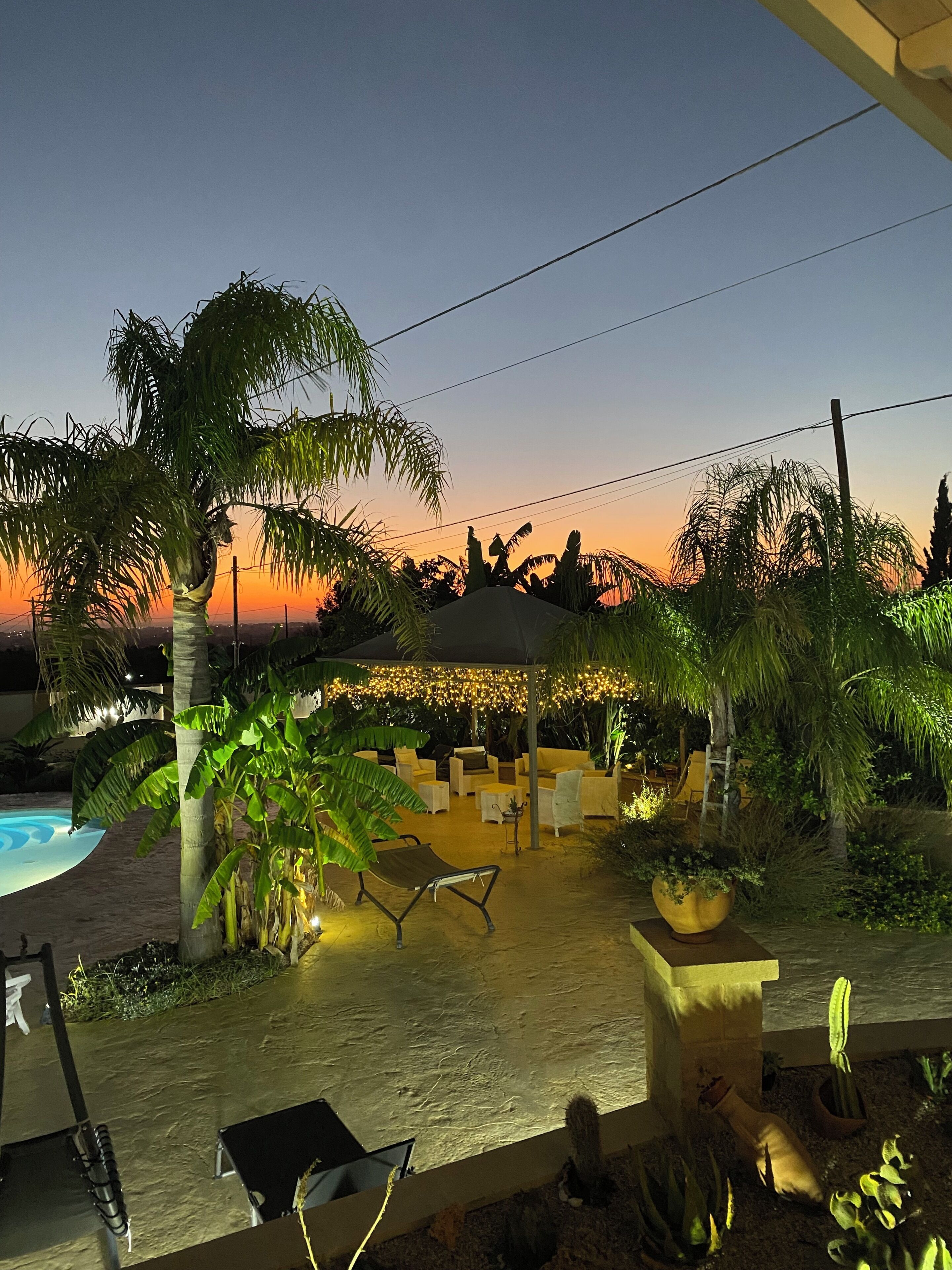 Eine Terrasse mit Gartenmöbeln, einem Pool und Blick auf den Sonnenuntergang.