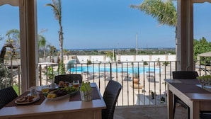 Un balcón con vista a la piscina, muebles de mimbre y una mesa con desayuno.