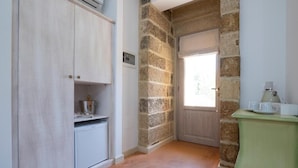 Un pasillo estrecho con pared de piedra, una puerta, un mueble blanco pequeño y una mesa verde con una taza y un platillo.