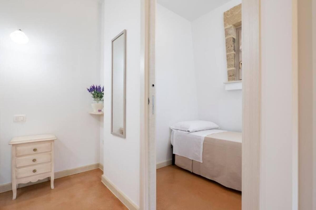 Un dormitorio con cama, mesita de noche, espejo y ventana con detalles de piedra.