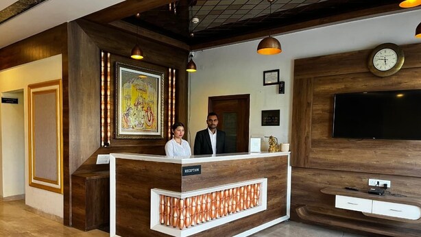 A reception desk with a wooden finish and a 'RECEPTION' sign, a clock, and a framed picture on the wall. - Sanskar Grand by Maan (Jaipur)