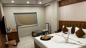 A hotel room with a large bed, a desk, a chair, a TV, and a window with a patterned curtain. - Sanskar Grand by Maan (Jaipur)