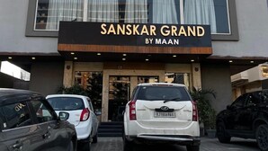 A hotel named 'SANSKAR GRAND BY MAAN' with a modern facade, a parking area with several cars, and a visible entrance. - Sanskar Grand by Maan (Jaipur)