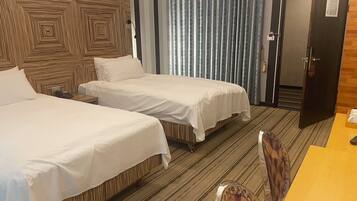 A hotel room with two beds, a wooden headboard, a striped carpet, a door, and a table with a chair.