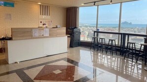En hotellobby med ett stort fönster som ger utsikt över staden, en receptionsdisk och en bardisk med barstolar.
