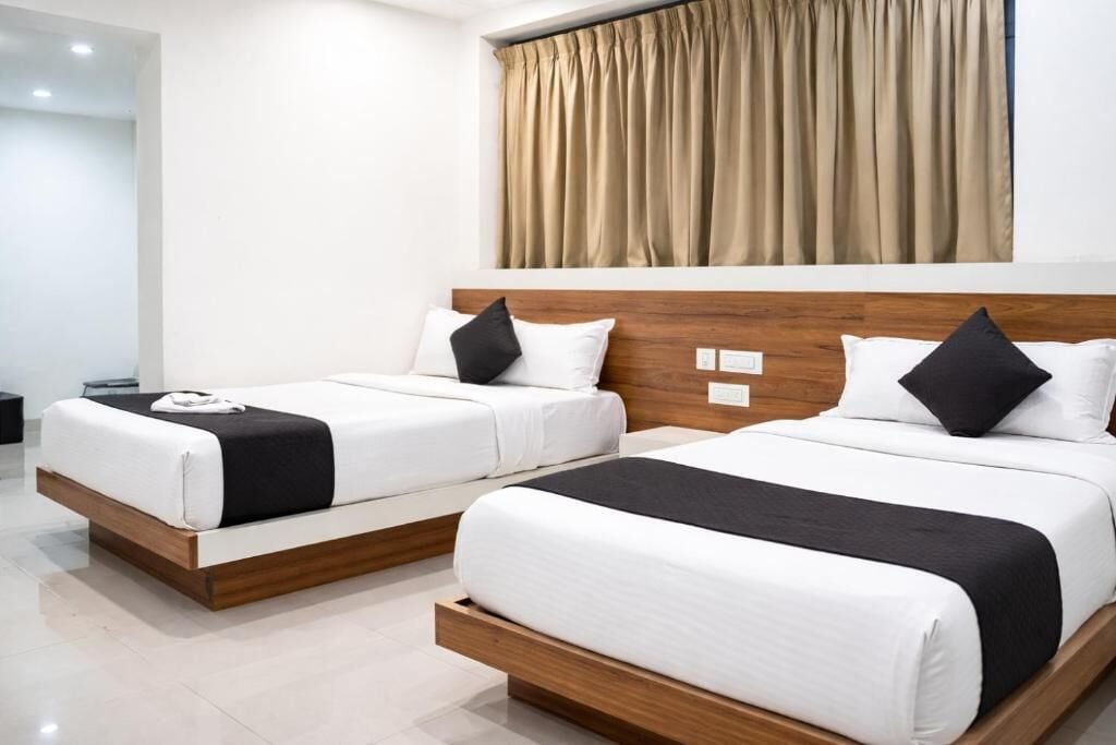 A hotel room with two beds, wooden headboards, white bedding, and a beige curtain.
