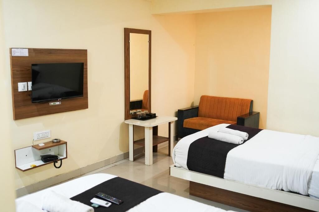 Une chambre d’hôtel avec un lit, une chaise, une petite table, une télévision et un miroir.
