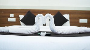 Una cama bien hecha con toallas dispuestas en forma de corazón, un control remoto y un pequeño dispositivo electrónico sobre la cama.