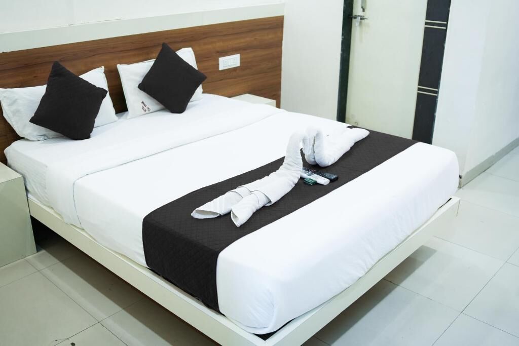 Una cama bien hecha con ropa de cama blanca y negra, un cabecero de madera y una mesita de noche blanca con una lámpara.