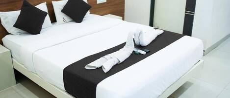 Una cama bien hecha con ropa de cama blanca y negra, un cabecero de madera y una mesita de noche blanca con una lámpara.