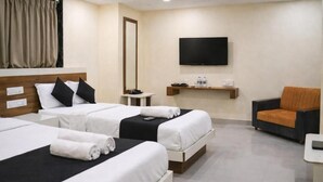 Una habitación de hotel con tres camas, un televisor, una mesita pequeña y una silla.