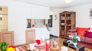 En kompakt opholdsstue med tekøkken, spiseplads med morgenmadsprodukter, sofa og reol.