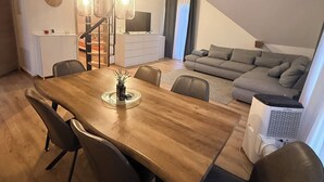 Un comedor con mesa y sillas de madera, una escalera, una sala de estar con sofá y televisor.
