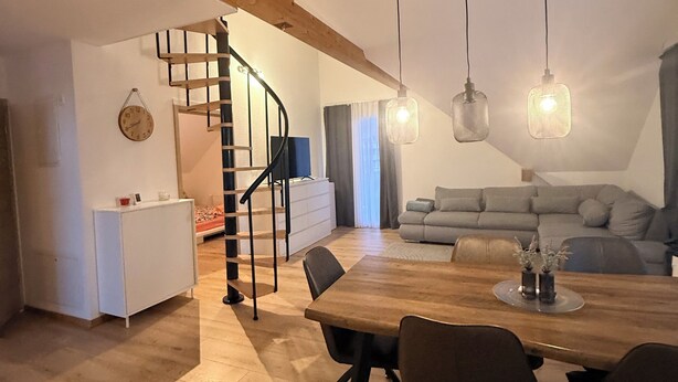 Un comedor amplio con una mesa y sillas de madera, una escalera y lámparas colgantes.