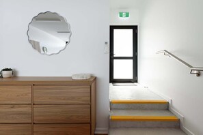 A staircase with yellow edges, a wooden dresser, a mirror, and a door with an emergency exit sign.