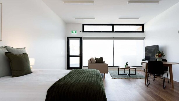 A modern hotel room with a large bed, a sofa, a dining table, and a TV.