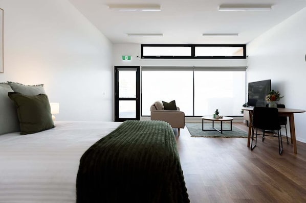 A modern hotel room with a large bed, a sofa, a dining table, and a TV.
