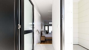 A hallway leading to a bedroom with a bed, bedside table, and a window.