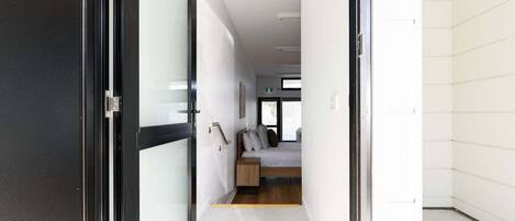 A hallway leading to a bedroom with a bed, bedside table, and a window.