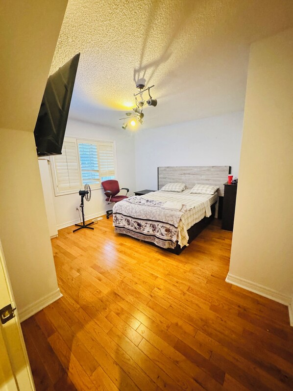 Une chambre à coucher comprenant un lit, une chaise, un bureau, un ventilateur de plafond et un téléviseur fixé au mur.