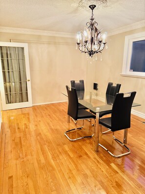 Un espace repas avec une table en verre et des chaises noires, un lustre, un plancher en bois et une porte dotée d’un panneau en verre.