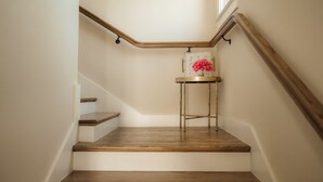 Un escalier avec des marches en bois et une rampe métallique, menant à un palier où se trouvent une petite table et un vase de fleurs.