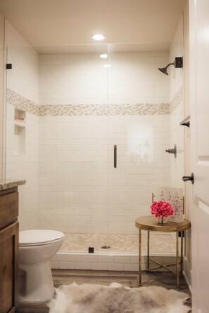 Un baño con inodoro, ducha y una pequeña mesa con un florero.