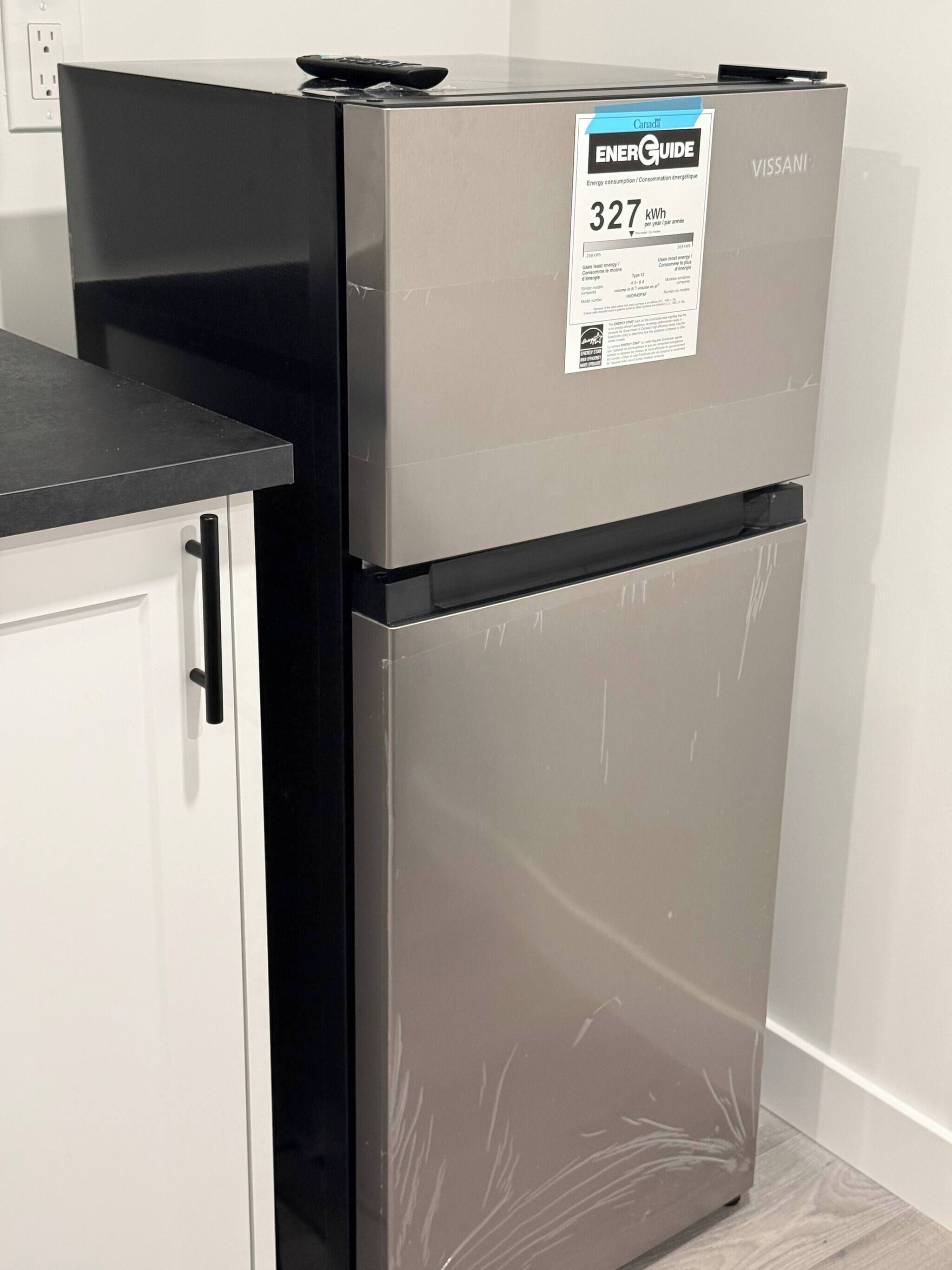 A stainless steel refrigerator with a ENERGY GUIDE label indicating 327 kWh per year, placed next to a white cabinet with a black handle.